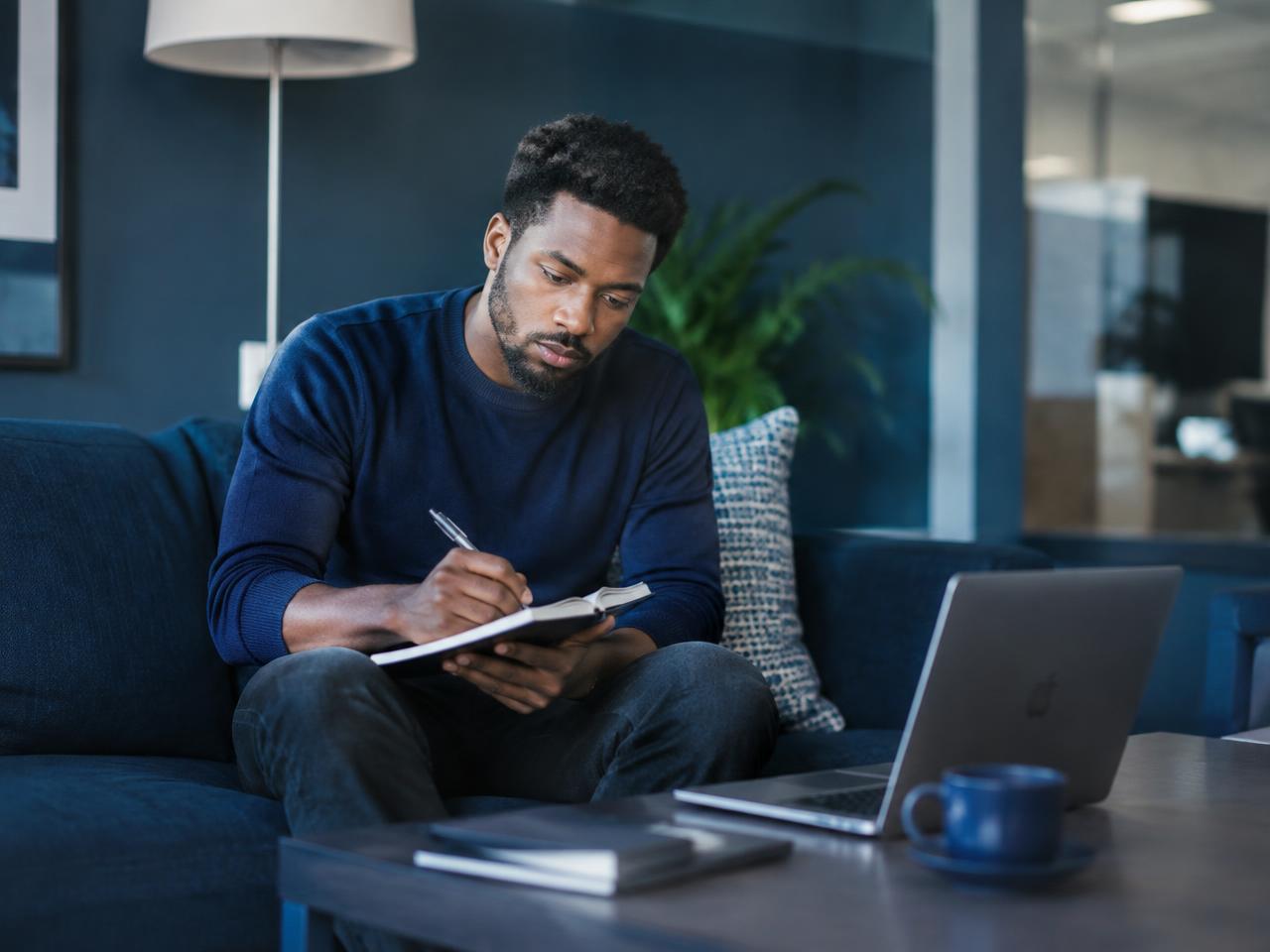 A professional studying with a notebook and laptop in a modern office lounge